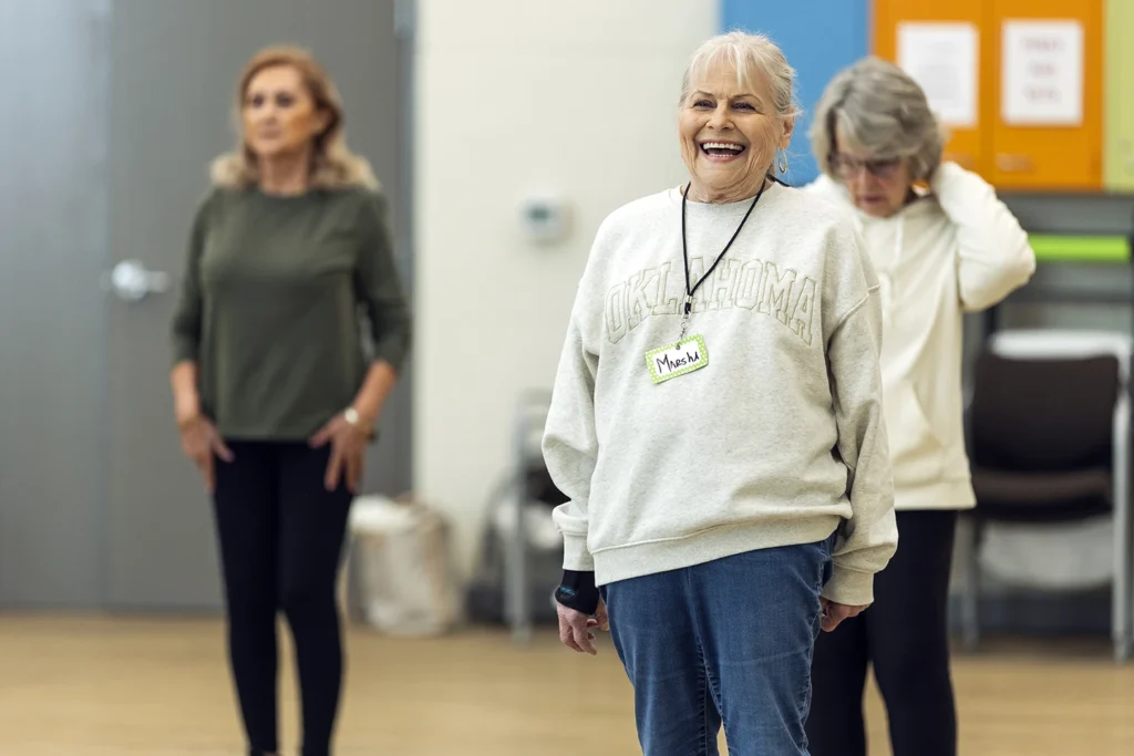 Smiling older woman named Marsha wearing an Oklahoma sweatshirt participates in a group exercise class