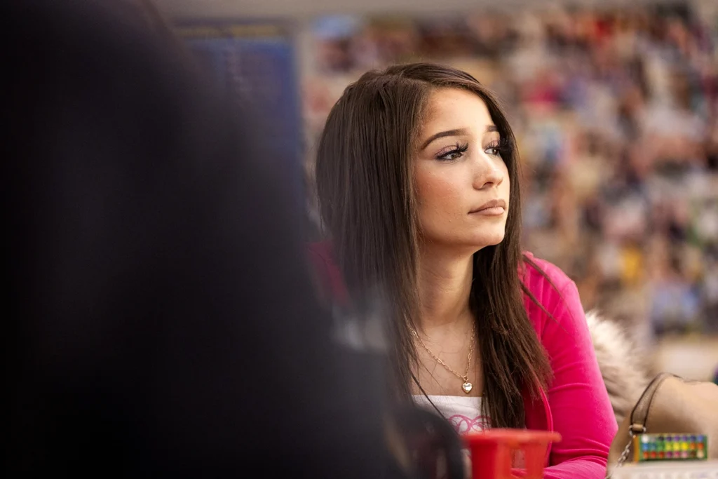 Young woman in pink top listening attentively at a crowded community event in Tulsa